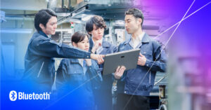 Diverse team in blue jackets collaborates in a workshop, using technology for problem-solving.